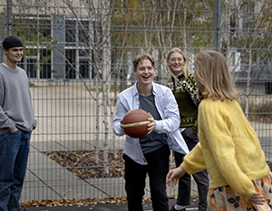 En gruppe unge voksne spiller basketball på en udendørs bane i byerne, smiler og interagerer legende. en spiller holder basketball og forbereder sig på at sende den.