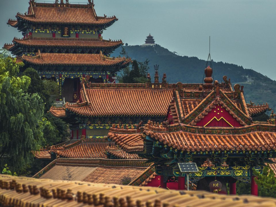 Traditionelle kinesiske templer med pagodetage i flere niveauer og indviklede udskæringer, beliggende i et frodigt, bakket landskab under en klar himmel.