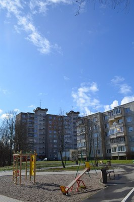 Legeplads med farverigt udstyr foran beboelsesejendomme under en klar blå himmel.